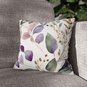 May include: A white throw pillow with a watercolor design of purple and green leaves and gold branches.