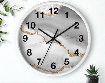 May include: White round clock with black hands and black numbers on a white background with gold glitter accents. The clock face has a marbleized design.