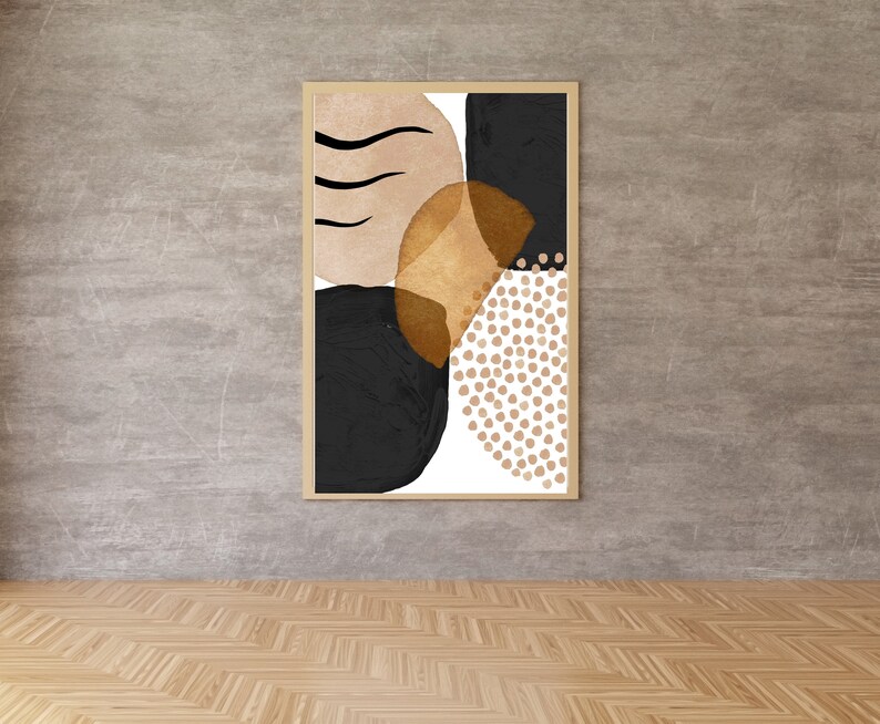 May include: Abstract art print in a light wood frame. The artwork features a composition of black, tan, and gold shapes, including a dotted pattern and curved lines. The art is displayed against a gray wall.