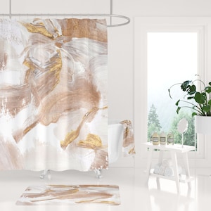 Puede incluir: Una cortina de ducha blanca con pinceladas abstractas marrones y doradas. La cortina de ducha est&aacute; colgada de una barra de ducha plateada. Se puede ver una ba&ntilde;era blanca en el fondo. Una alfombra de ba&ntilde;o blanca con un dise&ntilde;o abstracto similar est&aacute; en el suelo.