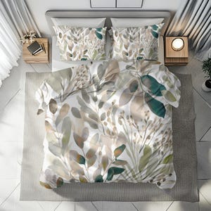 May include: A bed with a white duvet cover and two matching pillowcases, all featuring a watercolor design of green, beige, and brown leaves. The bedding is arranged on a gray bed frame, with two wooden nightstands on either side.