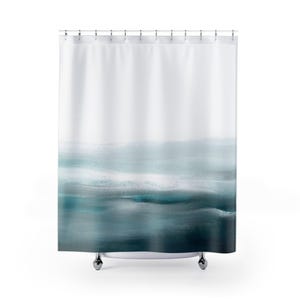 Op de afbeelding: Een witte douchegordijn met een abstract ontwerp. Het ontwerp heeft horizontale banden in verschillende tinten blauw en teal, waardoor een aquareleffect ontstaat. Het bovenste gedeelte is wit en gaat over in de blauwtinten.