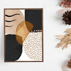 May include: Abstract art print in a dark wooden frame. The artwork features a composition of black, tan, and gold shapes, including a dotted pattern and curved lines. The overall design is modern and minimalist, suitable for home decor.