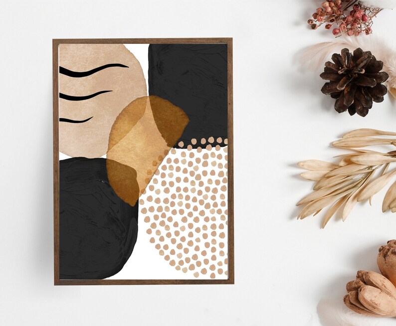 May include: Abstract art print in a dark wooden frame. The artwork features a composition of black, tan, and gold shapes, including a dotted pattern and curved lines. The overall design is modern and minimalist, suitable for home decor.
