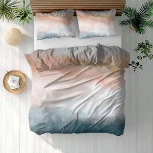 May include: A bed with a watercolor-style duvet cover and two pillowcases. The bedding features a gradient design with shades of peach, gray, white, and teal. The bed is surrounded by plants and decorative items, creating a serene aesthetic.