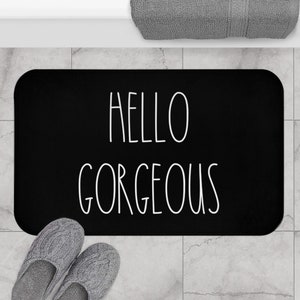 Puede incluir: Alfombra de baño negra con texto blanco que dice "hello gorgeous".