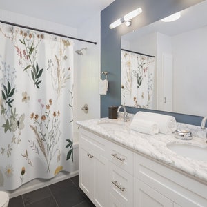 May include: A white bathroom with a floral shower curtain, a white vanity with two sinks, and a large mirror above the sinks.