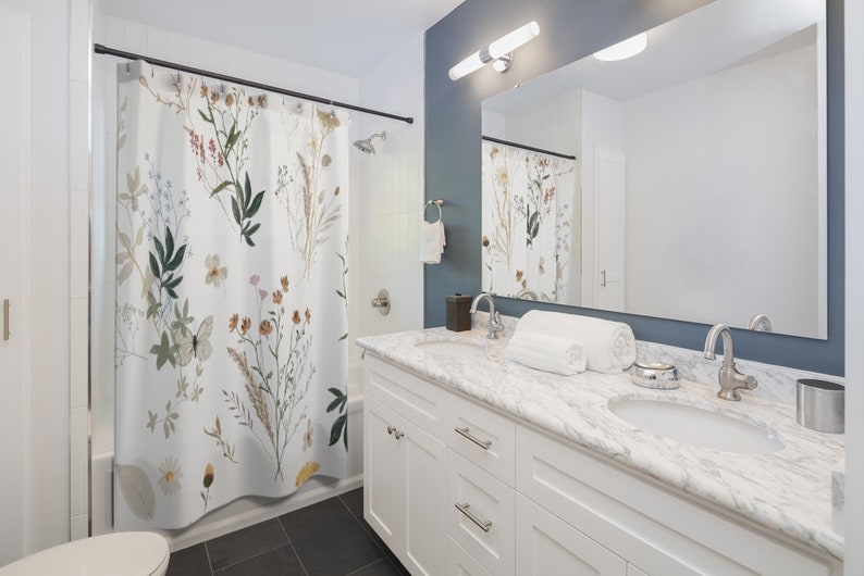 May include: A white bathroom with a floral shower curtain, a white vanity with two sinks, and a large mirror above the sinks.