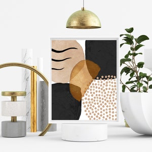May include: A framed abstract art print featuring a composition of black, tan, and gold shapes. The artwork includes curved lines, solid blocks, and dotted patterns on a white background. The print is displayed on a white pedestal.