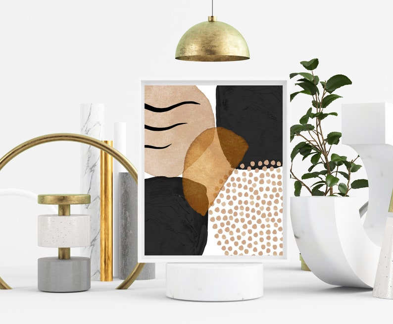 May include: A framed abstract art print featuring a composition of black, tan, and gold shapes. The artwork includes curved lines, solid blocks, and dotted patterns on a white background. The print is displayed on a white pedestal.