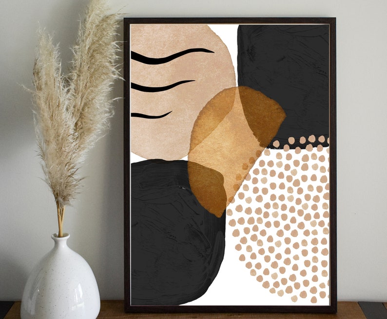 May include: Abstract art print in a dark wood frame. The artwork features black, tan, and gold shapes with a white background. The design includes organic shapes and dotted patterns, creating a modern aesthetic.