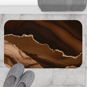 May include: A brown and gold abstract bath mat with a swirling pattern. The mat has a textured surface and is designed to absorb water.