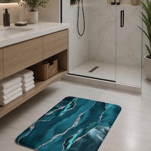 Puede incluir: Alfombra de baño abstracta en color turquesa y plateado. La alfombra rectangular presenta un diseño marmolado con tonos turquesa y turquesa fluidos, acentuados por líneas plateadas brillantes. La alfombra está colocada sobre un suelo de baldosas blancas en un baño.
