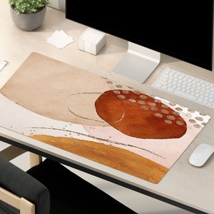 May include: A brown, beige, and pink abstract design desk mat with gold glitter accents. The mat features a large, rounded, orange-brown shape with white dots.