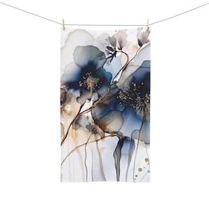 K&ouml;nnte beinhalten: Ein rechteckiges wei&szlig;es Handtuch mit einem Aquarell-Blumenmuster. Das Kunstwerk zeigt gro&szlig;e, abstrakte blaue und graue Blumen mit goldenen Akzenten und zarten Stielen. Das Handtuch h&auml;ngt an einer W&auml;scheleine.