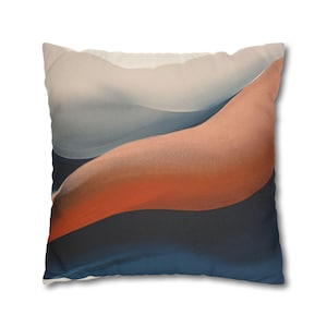 Peut inclure: Coussin carré avec un motif abstrait. Le coussin présente un dégradé de couleurs, dont le blanc, l'orange et le bleu foncé. Le motif ressemble à des formes fluides ou à des dunes, créant une esthétique moderne et artistique. Le coussin est probablement en tissu doux.