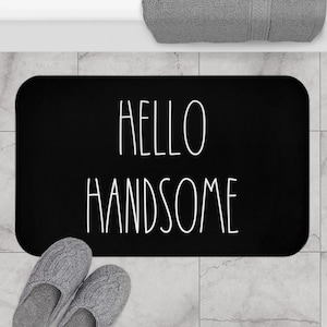 Puede incluir: Alfombra de baño negra con texto blanco que dice "Hello Handsome".