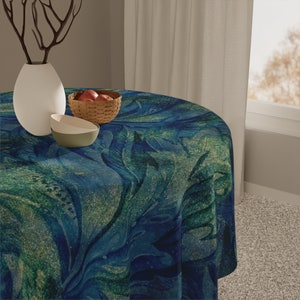 May include: A round blue and green tablecloth with a swirling abstract pattern. The tablecloth is on a table with a white vase and a bowl of fruit.