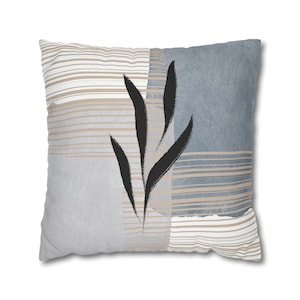May include: A decorative throw pillow with a geometric pattern in shades of gray and beige. The pillow features a black stylized leaf design.