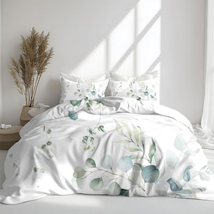 May include: White bedding set with a botanical design featuring green and blue eucalyptus leaves and branches. The set includes a duvet cover and two pillowcases. The design is a watercolor style, creating a soft and natural aesthetic.