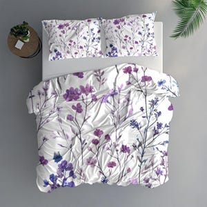 Peut inclure: Ensemble de literie blanc avec un motif floral dans des tons violets et bleus. L'ensemble comprend une housse de couette et deux taies d'oreiller. Le motif floral présente des tiges et des fleurs délicates, créant une esthétique douce et accueillante.