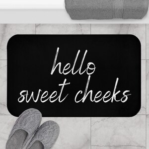 Puede incluir: Alfombra de baño negra con texto blanco que dice "hello sweet cheeks".