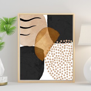 May include: Abstract art print in a wooden frame. The artwork features a composition of black, tan, and gold shapes, including circles, dots, and brushstrokes. The overall design is modern and minimalist, suitable for home decor.
