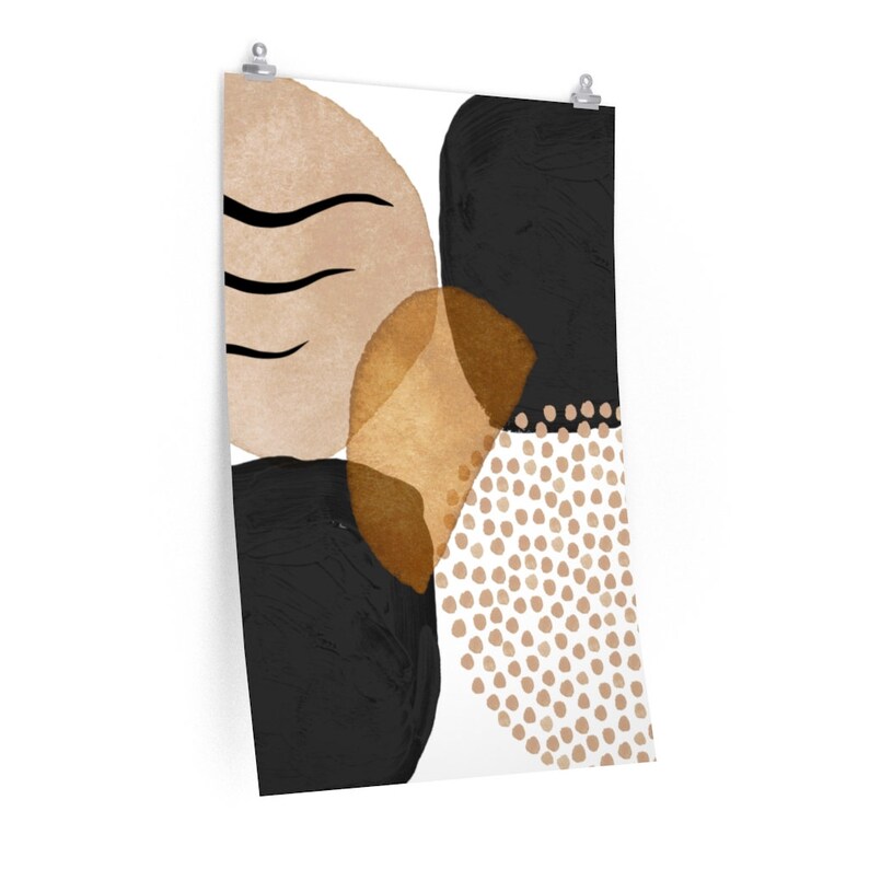 May include: Abstract art print featuring a composition of shapes in black, beige, and gold. The design includes curved lines, solid shapes, and a dotted pattern, all set against a white background. The artwork is mounted with clips.