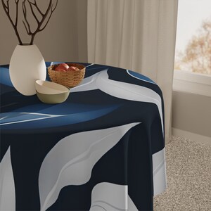 Pode incluir: Uma toalha de mesa redonda azul e branca com um padrão de folhas. A toalha de mesa está drapeada sobre uma mesa com um vaso e uma tigela de frutas no topo.
