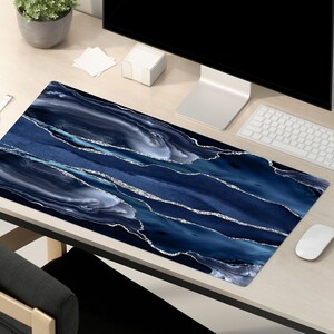 May include: A blue and silver marble desk mat with a modern abstract design. The mat is on a light wood desk with a computer, keyboard, mouse, and other office supplies.