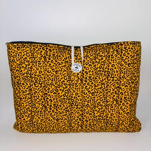 May include: A rectangular, quilted bag with a yellow leopard print pattern. The bag has a black zip and a white cord closure with a small, round tag that reads "Handmade with love."
