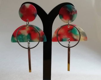 May include: Abstract earrings with a red, green, and white marbled pattern. Each earring features a circular top, a semi-circle, a silver hoop, and a gold-coloured rectangular bar. The earrings are displayed on a black stand.