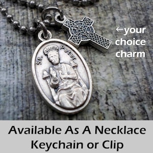 May include: Silver chain necklace with a silver oval pendant featuring a depiction of Saint Peter and a silver Celtic cross charm. The pendant has the words "St. Peter" inscribed on it. Available as a necklace, keychain, or clip.