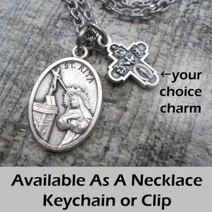May include: Silver St. Rita medal with a silver cross charm. The medal features a depiction of St. Rita with a crown of thorns and a sword. The cross charm has four medallions with images of saints. The text "ST. RITA" is visible on the medal. Available as a necklace, keychain, or clip.