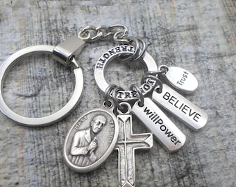 May include: Silver charm necklace or keychain with a silver cross, a silver oval charm with a man's face, and several silver tags with the words "Trust", "Believe", "Willpower", and "Strength".
