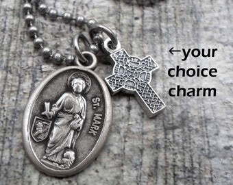 Può includere: Collana d'argento con un ciondolo ovale di San Marco e un ciondolo a croce celtica. La collana è su una catena a sfera d'argento. Collana, portachiavi o clip.