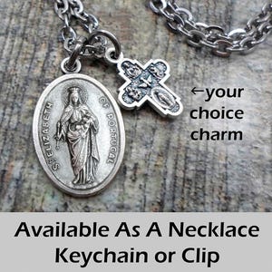 May include: A silver-toned necklace with two charms. One charm is an oval pendant with the image of St. Elizabeth of Portugal. The other is a cross-shaped charm. The text "Available As A Necklace Keychain or Clip" is at the bottom.