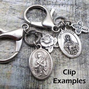 Pu&ograve; includere: Portachiavi in argento con diversi ciondoli, tra cui una rosa, una croce e due medaglioni ovali con figure religiose. I medaglioni raffigurano Santa Veronica e Santa Maria Goretti. Il testo "Santa Veronica" e "Santa Maria Goretti" &egrave; visibile sui medaglioni. Il portachiavi &egrave; un ottimo regalo per una persona religiosa.