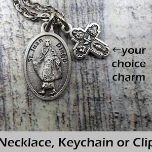 May include: A silver-toned necklace with two charms. One charm is an oval pendant with the text "St. Juan Diego" and an image of a saint. The other charm is a cross. The text "Necklace, Keychain or Clip" is at the bottom.