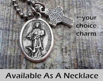 Può includere: Una collana color argento con due ciondoli. Un ciondolo è un pendente ovale con l'immagine di San Giovanni Evangelista. L'altro è un ciondolo a forma di croce. Il testo "Available As A Necklace Keychain or Clip" è in basso.