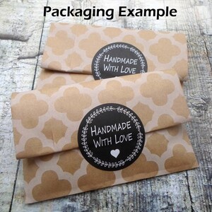 Pu&ograve; includere: Due pacchi di carta marrone con un motivo bianco. Ogni pacco ha un adesivo circolare bianco e nero che dice "Handmade with Love" con un cuore bianco al centro.