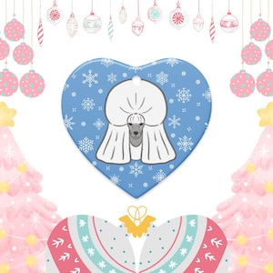 Könnte beinhalten: Herzförmiger Weihnachtsschmuck mit einer weißen Pudel-Illustration auf hellblauem Hintergrund mit Schneeflocken. Der Anhänger hat ein Loch zum Aufhängen und ist von festlichen Weihnachtsdekorationen umgeben, darunter rosa und weiße Kugeln.