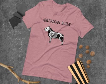 May include: A pink t-shirt with the text "AMERICAN BULLY" in black lettering and a skeleton image of an American Bully dog.