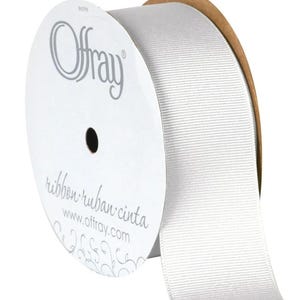 Könnte beinhalten: Eine Spule weißen Satinbandes mit dem Markennamen Offray und der Website auf dem Etikett. Das Band ist 1,5 Zoll breit.