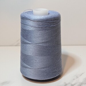 May include: A spool of light blue thread, tightly wound around a white plastic core. The thread has a subtle sheen, suggesting a smooth texture. Ideal for sewing, embroidery, or other textile crafts.