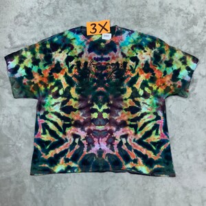 May include: A tie-dye t-shirt with a colorful, abstract pattern in shades of green, orange, yellow, blue, and purple. The shirt has a black silhouette of a group of people on the front.