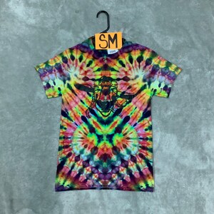 May include: A tie-dye t-shirt with a colorful swirl pattern in shades of pink, yellow, green, blue, and purple. The shirt features a black and white graphic of a goat wearing a hat and sunglasses.