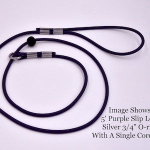 May include: A purple slip lead for dogs, featuring a 5-foot length, a silver 3/4" O-ring, and a single cord lock. The lead is made of a durable, flexible material, designed for secure and comfortable handling during walks and training.