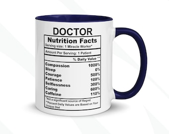 Op de afbeelding: Een witte keramische koffiemok met een blauwe rand en handvat. De mok heeft een voedingswaarde-etiket met de titel "DOCTOR" en een lijst met eigenschappen met percentages, zoals "Mededogen 1000%", "Slaap 0%", "Moed 500%", "Geduld 100%", "Ongeïnteresseerdheid 300%", "Zorg 600%" en "Cafeïne 110%".