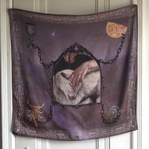 May include: A square purple scarf featuring a central gothic arch frame containing a hand touching a white goat. The corners display a chalice, a pomegranate slice, a scorpion, and a seashell, all connected by black chains to the central frame.